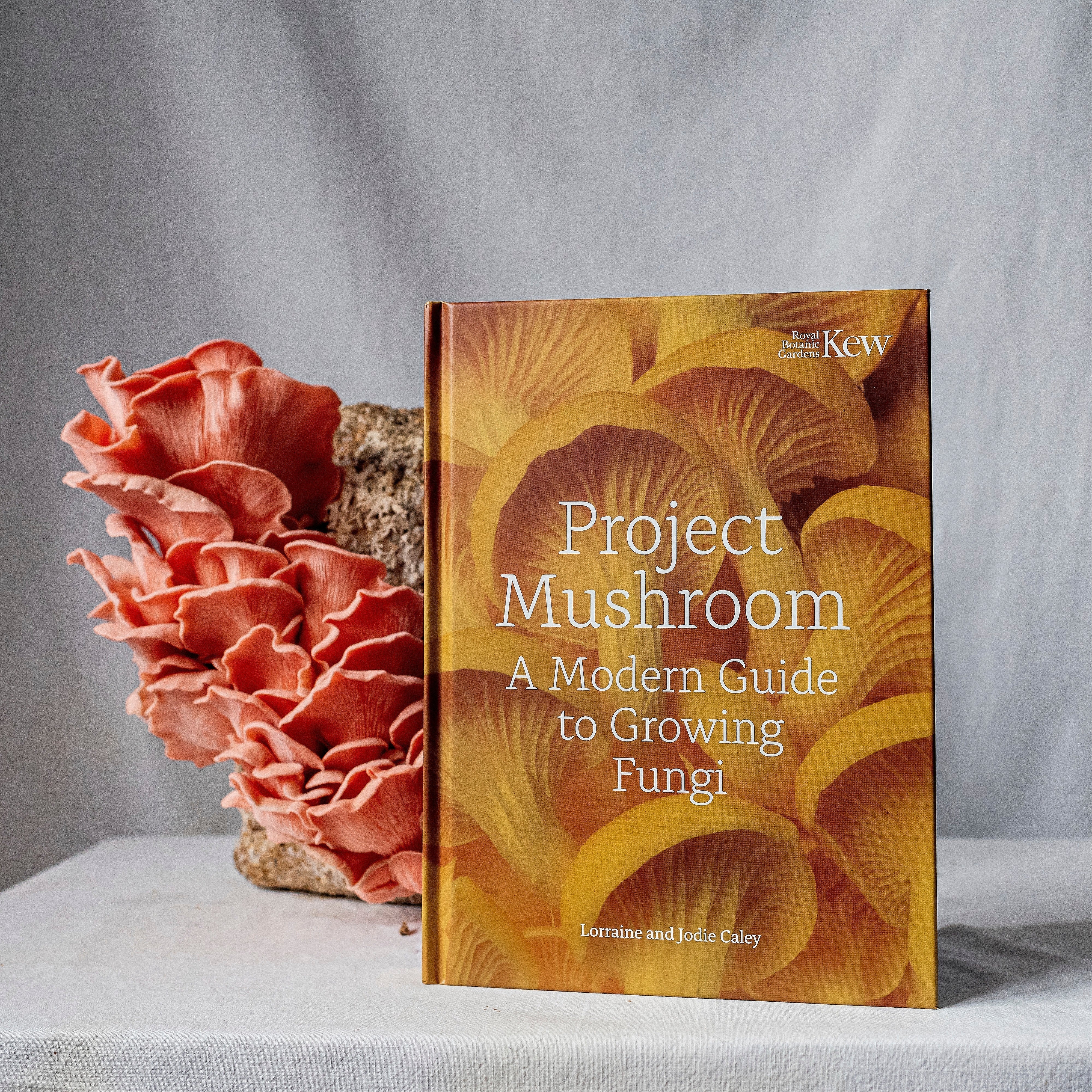 An imaged of our book Project Mushroom, with pink oyster mushrooms in the back ground.
