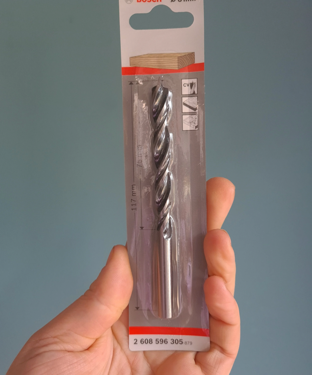 Drill bit in packaging held by a hand against a gray background