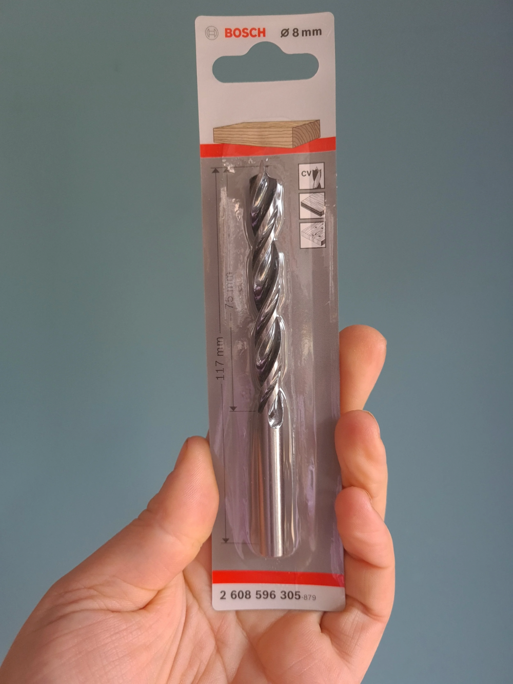 Drill bit in packaging held by a hand against a gray background