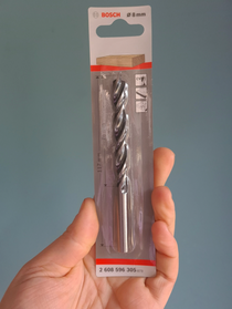 Drill bit in packaging held by a hand against a gray background