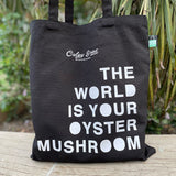 Black tote bag with white text on a wooden surface with plants in the background