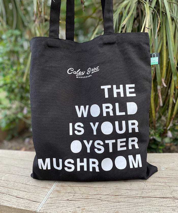Black tote bag with white text on a wooden surface with plants in the background